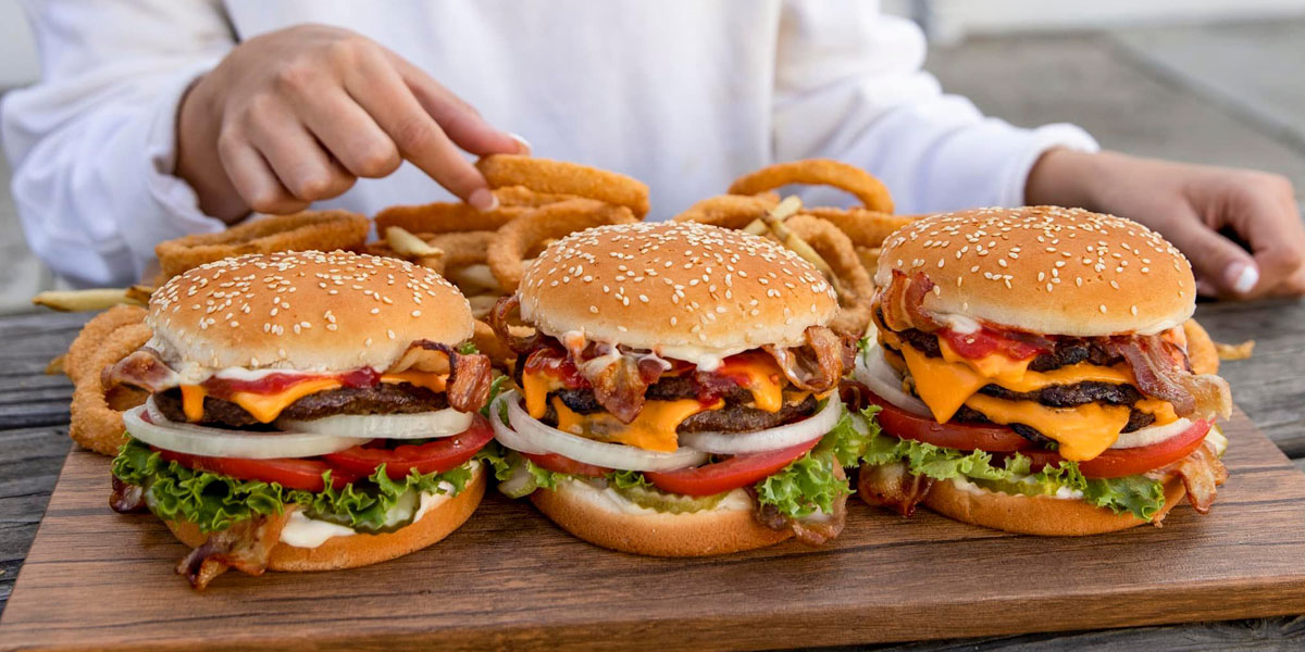 Three large Carl's Jr. cheese burgers on a wood tray with onion rings