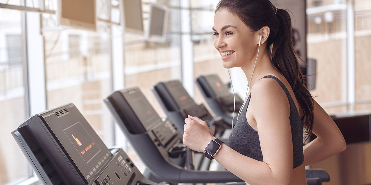 Attractive brunette woman running on a treadmill with headphones in ear.