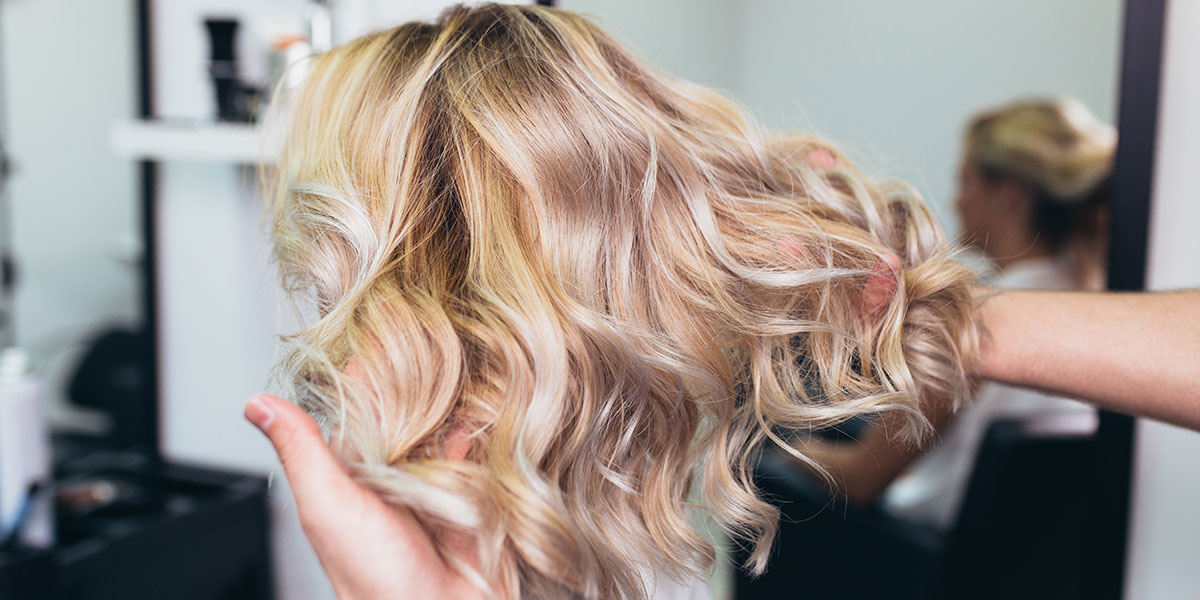 Woman showing off newly colored and curled hair in a salon chair.