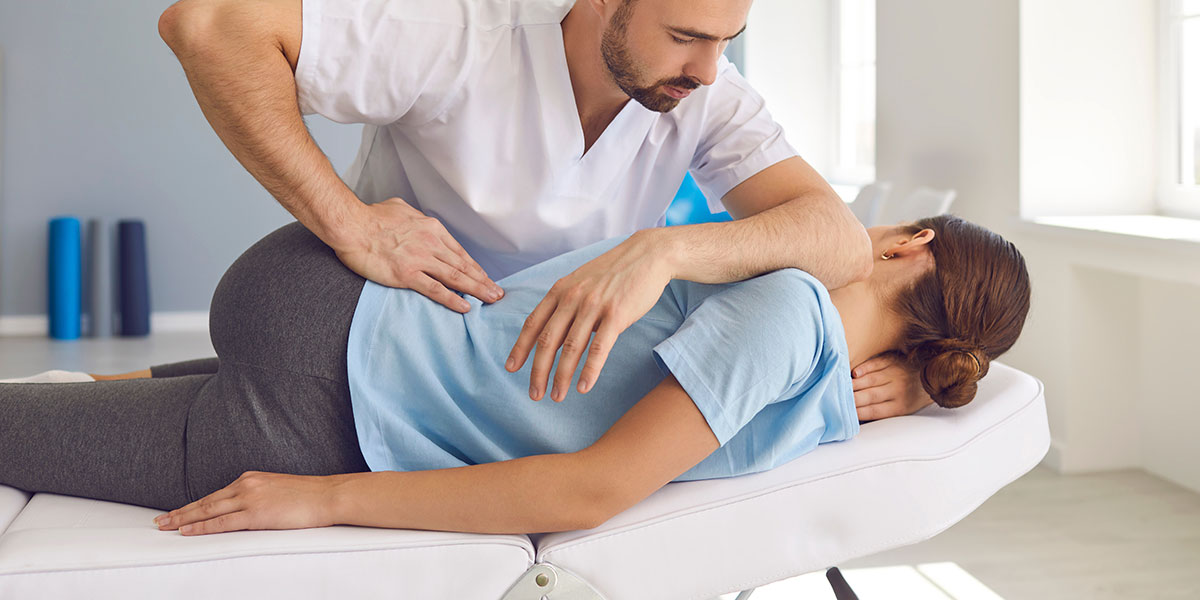 Chiropractor giving an woman a back adjustment on a table.