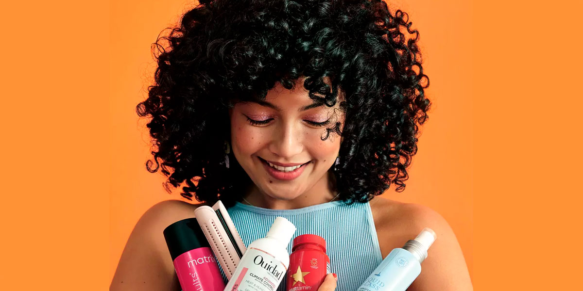 Attractive woman with thick, black curly hair holding various hair care products.