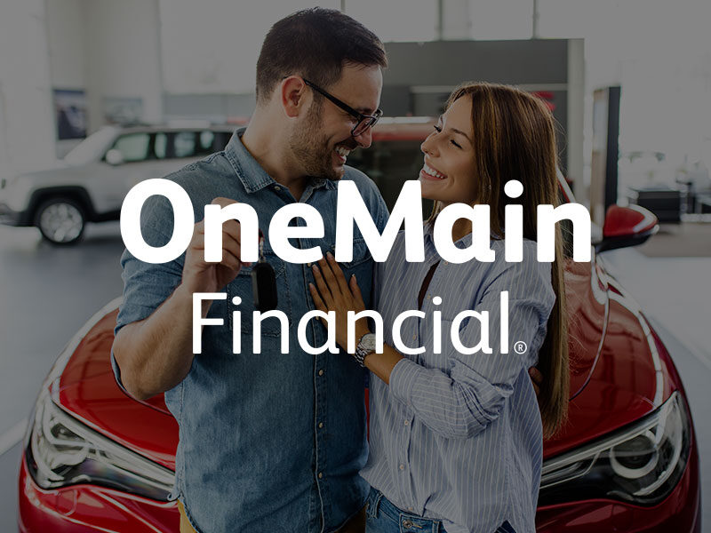 OneMain Financial logo over an image of a Man holding new car keys with a woman hugging him in front of a red car.