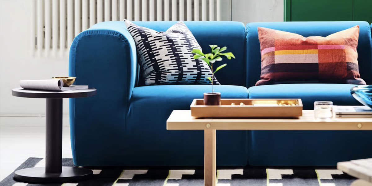 Modern living room scene featuring a blue sofa, patterned pillows, coffee table, and side table with IKEA-style home décor.